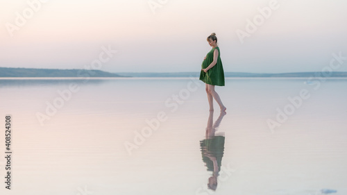 Pregnant girl posing at sunset in the water with a reflection