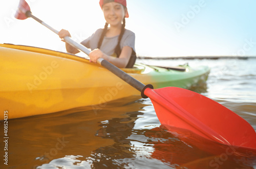 Little girl kayaking along river, focus on paddle. Summer camp activity