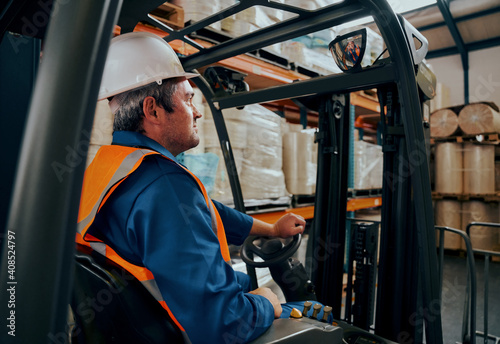 Side shot of a male worker driving the forklift truck in the warehouse