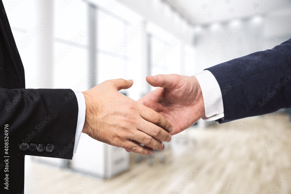 Obraz premium Handshake of two businessmen on the background of modern furnished office, partnership concept, close up