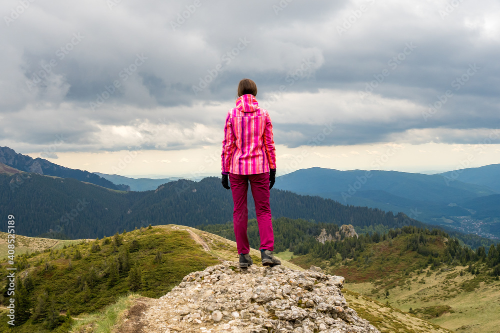 Dramatic landscape with a hiking girl standing on top of a mountain looking into the distance at the beautiful valleys and hills of the Carpathian mountains.