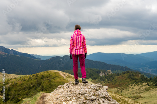 Obraz na płótnie Dramatic landscape with a hiking girl standing on top of a mountain looking into the distance at the beautiful valleys and hills of the Carpathian mountains. w salonie