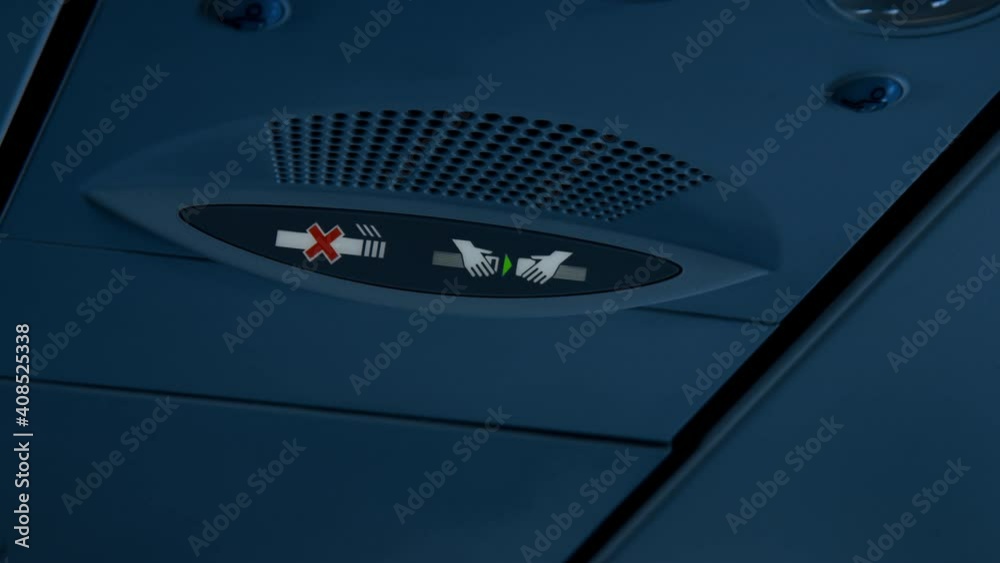 Seat belt notification signal light turns off and on inside dark lit passenger airplane cabin. Flight safety regulations and procedures in modern aviation rules