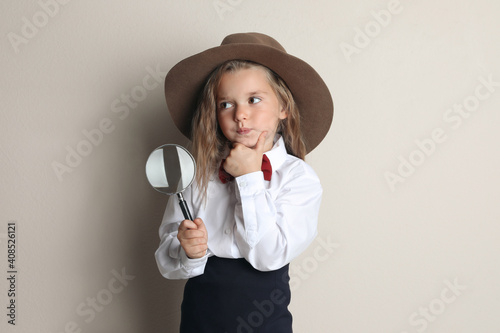 Cute little child in hat with magnifying glass playing detective on beige background