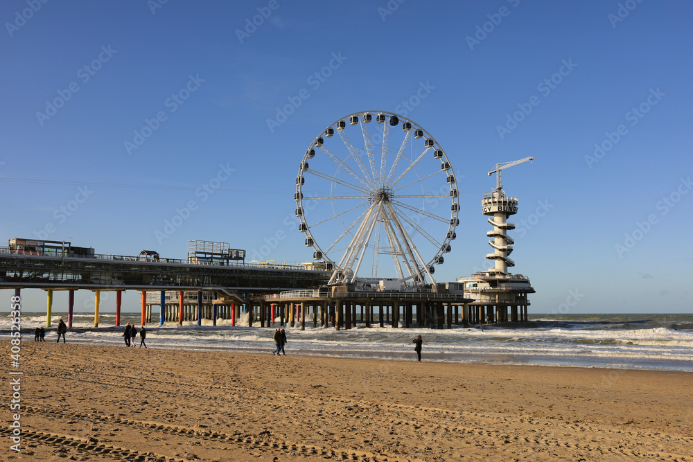 Ferris wheel on De Pier in The Hague Scheveningen on a windy winter day with blue sky and people at the beach, the Netherlands, Europe