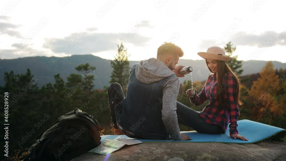 A young woman and a man are sitting on a large rock. A man is pouring tea into a cup. Sunset, mountain hike. 4K. A young woman and a man are sitting on a large rock. A man is pouring tea into a cup. Sunset, mountain hike. 4K.