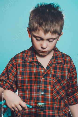 A boy in pajamas brushes his teeth, oral hygiene from childhood is especially important. The boy with disgust and grimace at the toothpaste looks at the brush. photo