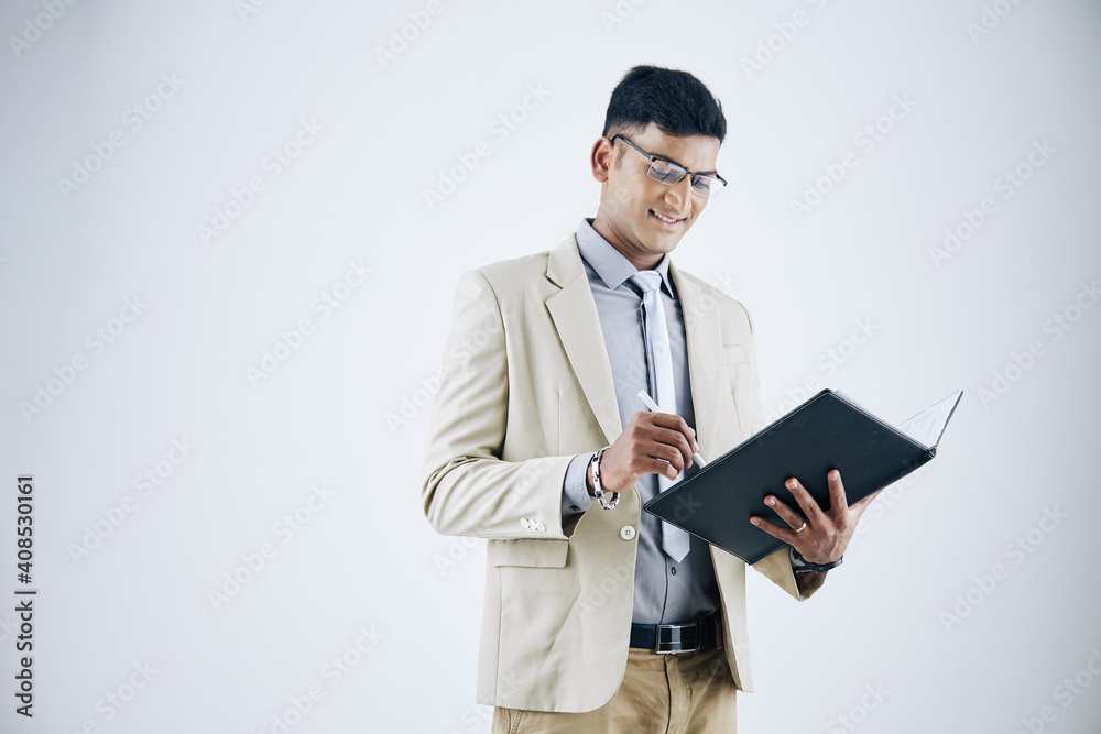 Portrait of smiling successful young Indian businessman filling document in lether folder