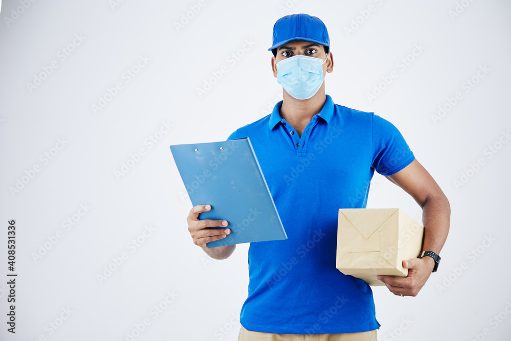 Portrait of serious confident young delivery man in medical mask holding document and package Portrait of serious confident young delivery man in medical mask holding document and package