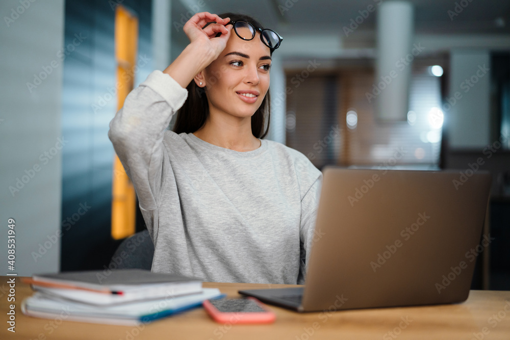 Happy young woman in eyeglasses smiling while working with laptop Happy young woman in eyeglasses smiling while working with laptop