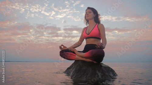 Young woman meditating in pose of lotus on sand beachat sunset photo