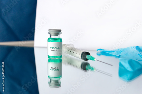 Development and creation of a coronavirus vaccine COVID-19. Ampoule, syringe and blue gloves on white reflective surface. Healthcare and medical concept.