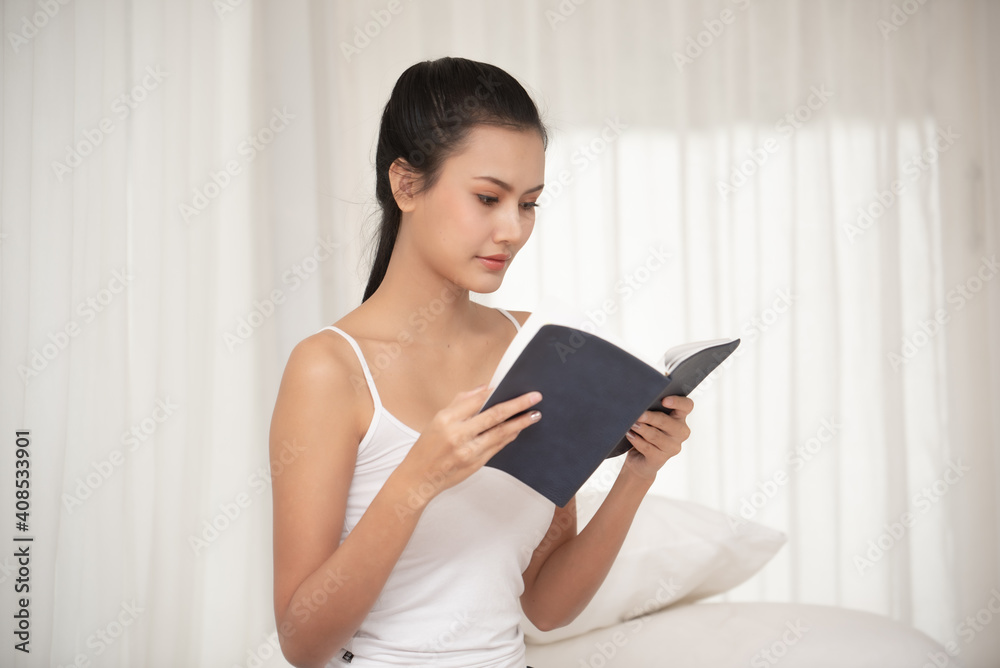 Young Woman Reading Book While Sitting On Bed Young Woman Reading Book While Sitting On Bed
