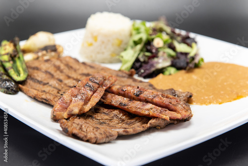 Grilled carne asada steak topped with chorizo served on a plate with rice and beans.
