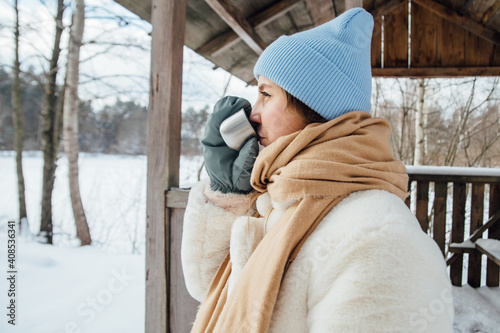 beautiful girl in a white fur coat drinks warm tea in winter in a snowy forest