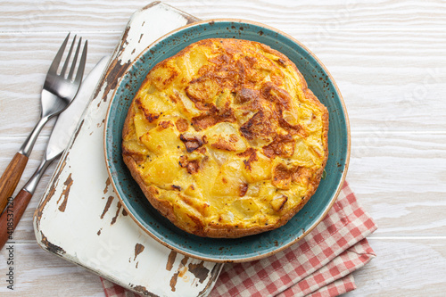 Homemade Spanish tortilla - omelette with potatoes on plate on white wooden rustic background top view. Traditional dish of Spain Tortilla de patatas for lunch or snack, overhead 