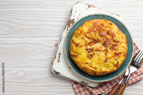 Homemade Spanish tortilla - omelette with potatoes on plate on white wooden rustic background top view. Traditional dish of Spain Tortilla de patatas for lunch or snack, overhead. Space for text 
