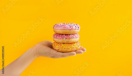 round pink and yellow very appetizing glazed doughnuts with sprinkles on palm of light-skinned person on bright yellow background. Order and deliver food online, food blog content, selective focus
