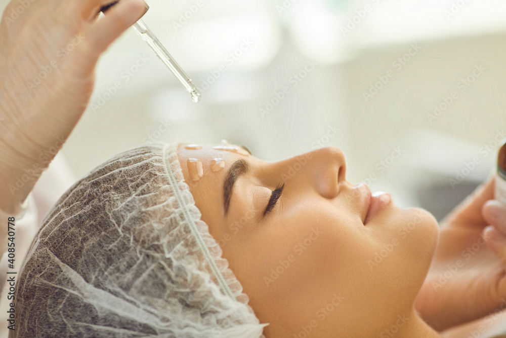 Smiling womans face getting skincare procedure of applying nourishing oil on skin