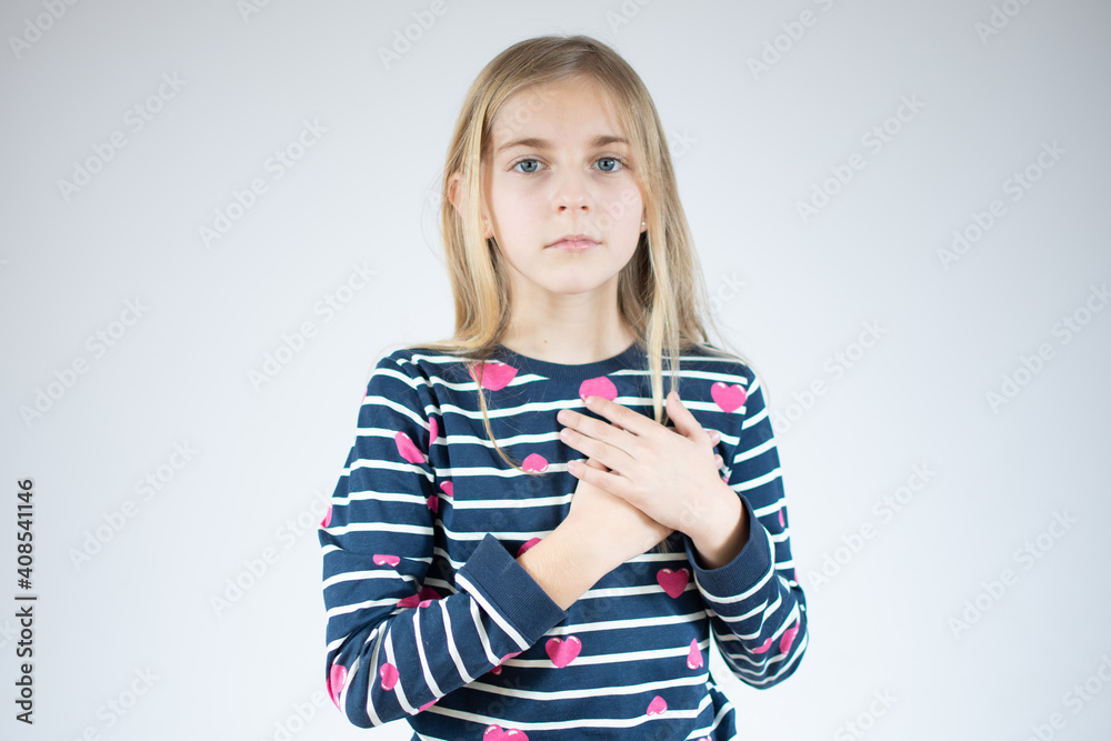 Little sincere girl holding hands on chest feeling gratitude pose isolated over white background. Little sincere girl holding hands on chest feeling gratitude pose isolated over white background.