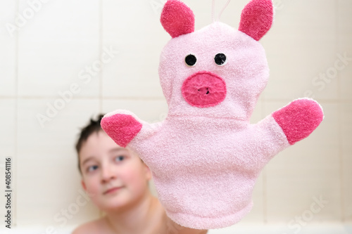 A boy in a bathroom showing funny piggy hand puppet toy washcloth close up, happy washing and shower concept photo