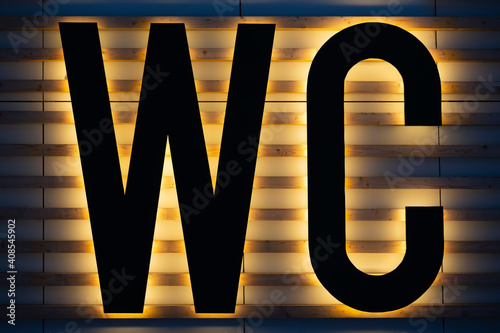Yellow backlit black WC sign on wooden strips wall