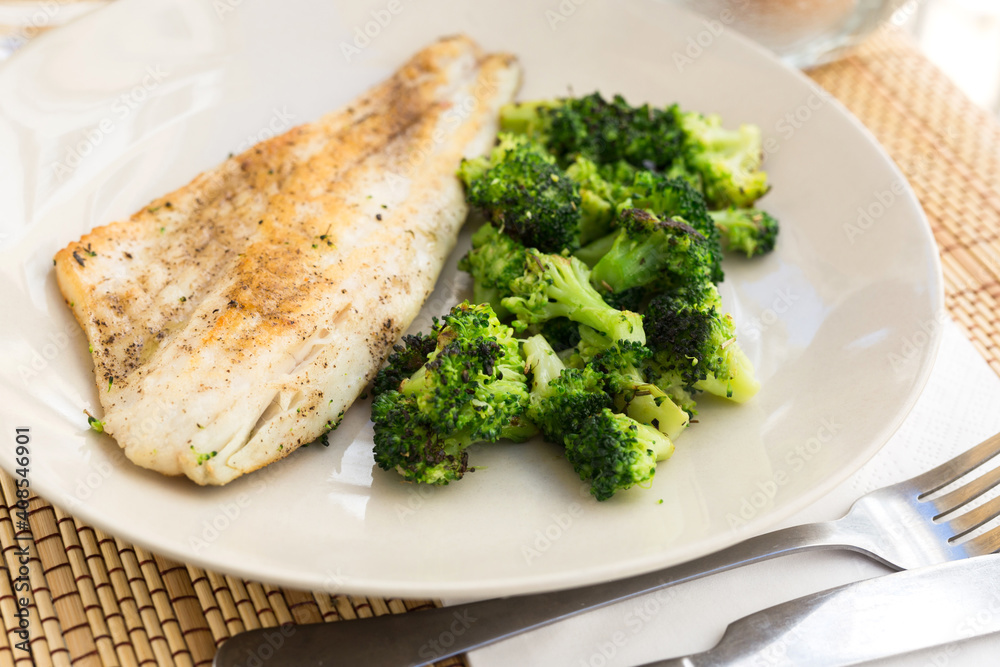 fried fillet of sea bass with garnish of broccoli on black warm stone plate fried fillet of sea bass with garnish of broccoli on black warm stone plate