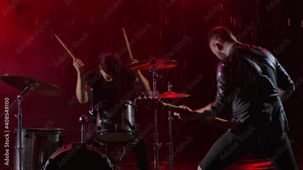 Camera slides over a group of rock musicians who play their instruments with crazy emotions in a dark studio illuminated by red lights. Drum set, electric and bass guitar. Close up. Slow motion. Camera slides over a group of rock musicians who play their instruments with crazy emotions in a dark studio illuminated by red lights. Drum set, electric and bass guitar. Close up. Slow motion.