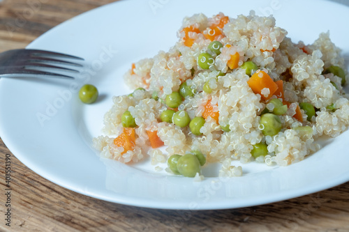 Quinoa porridge with vegetables and avocado in a white flat plate on a wooden board. Superfoods concept and top view.