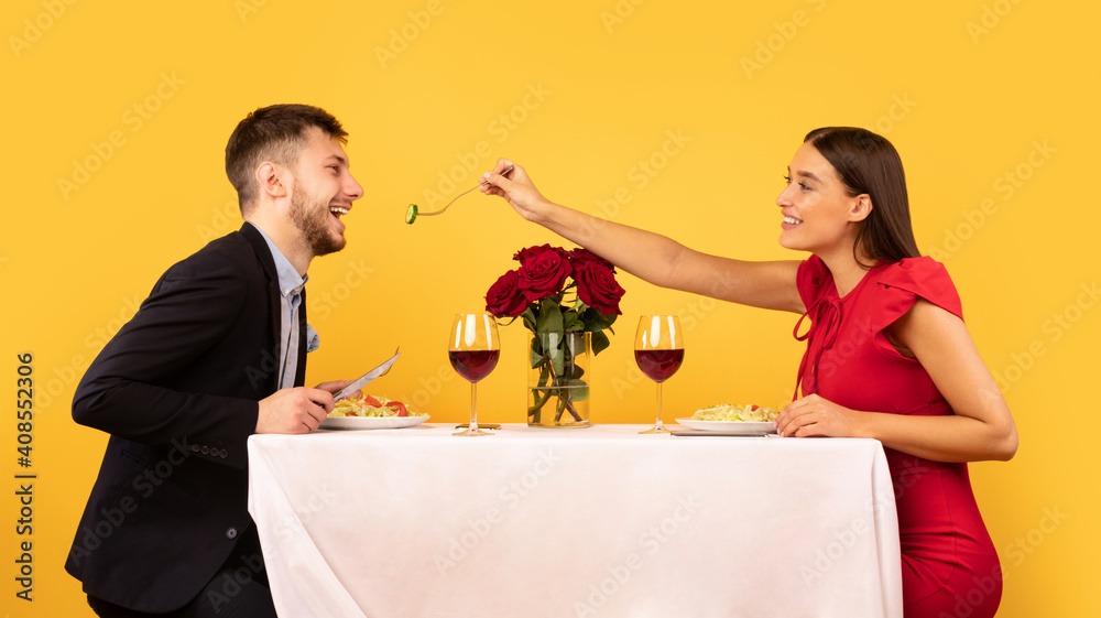 Loving Couple Feeding Each Other During Date On Yellow Background Loving Couple Feeding Each Other During Date On Yellow Background