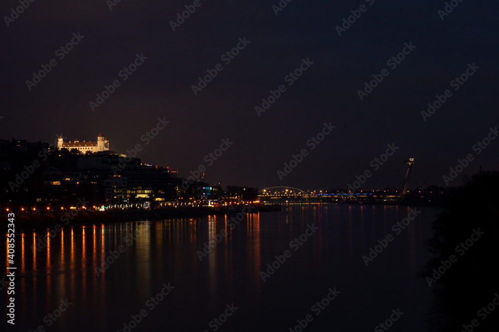 Beautiful view at bratislava city in the dark with glowing lights on the river water with bridge and castle in the background. Night scenery panorama.