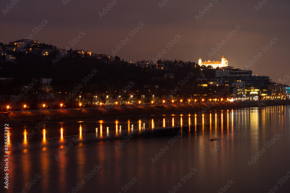 Night magical beautiful view at Bratislava city with glance of lights on Danube river and highlighted Bratislava castle in the background.