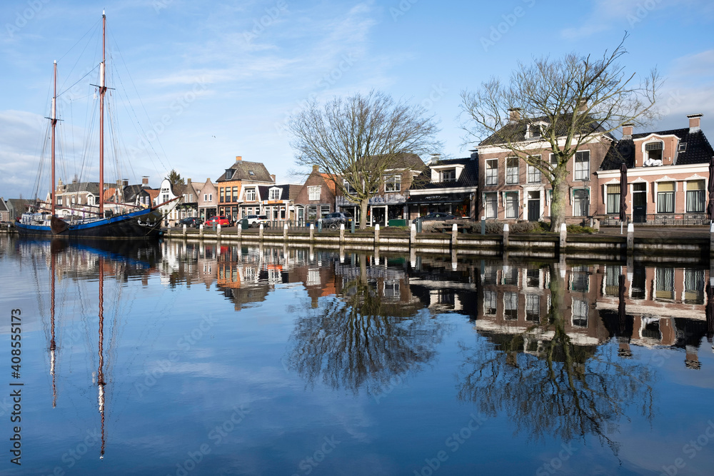 Cityscape of Lemmer with the sailing yacht with two masts and houses mirrored in the water of the Dok in the Netherlands