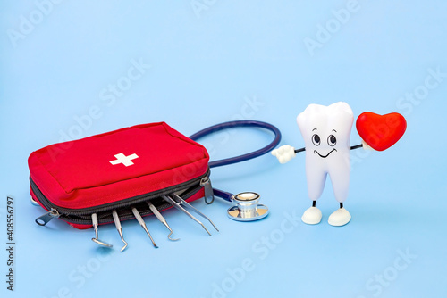 a cartoon model of a tooth with a heart in its hands and a first aid kit with dental instruments on a blue background. Love of oral hygiene photo