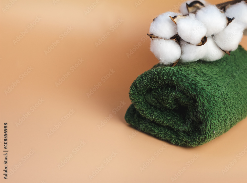 green, terry towel on a beige background, with a branch of cotton, close-up. Spa treatments green, terry towel on a beige background, with a branch of cotton, close-up. Spa treatments