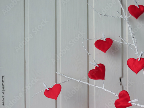 Red hearts on a white twig on a white wooden background.