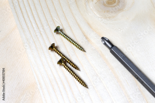 a bit for a screwdriver and a few self-tapping screws lie on a piece of wood. close-up.