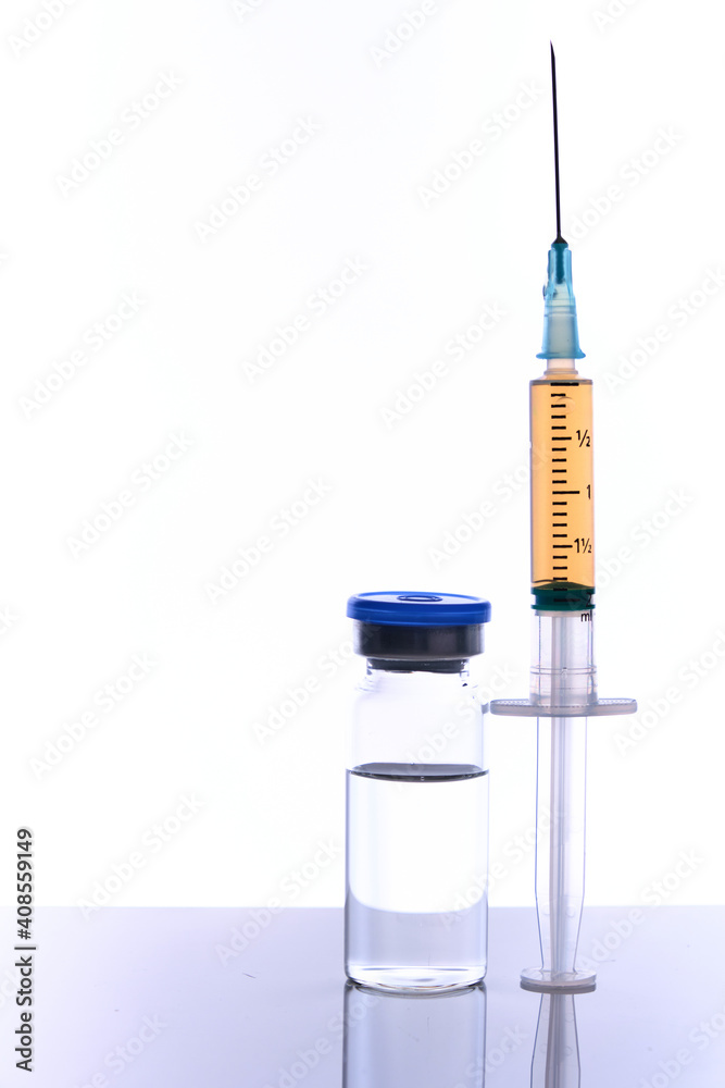 Medical vial vaccine dose and syringe on mirror surface, white backdrop, selective focus