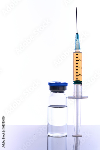 Medical vial vaccine dose and syringe on mirror surface, white backdrop, selective focus