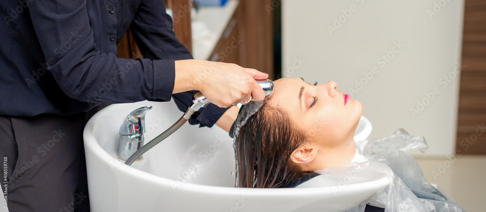 A female hairdresser is rinsing the hair of a young woman in a sink after shampooing in a hair salon A female hairdresser is rinsing the hair of a young woman in a sink after shampooing in a hair salon