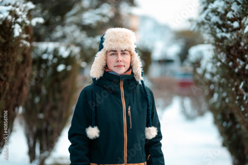 Portrait of a young Caucasian woman in a jacket and a hat with earflaps, posing in a snow-covered alley photo