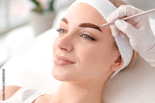 Tablou canvas Young woman undergoing eyebrow correction procedure in beauty salon