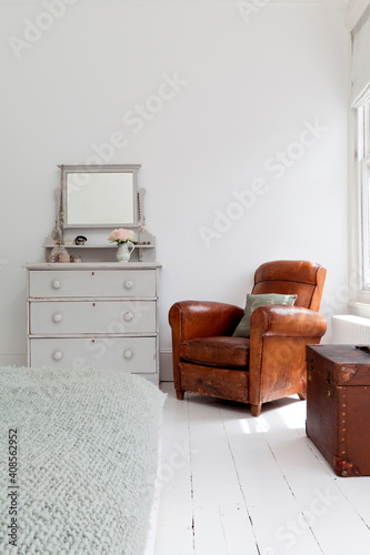 Brown leather armchair in corner of white bedroom
