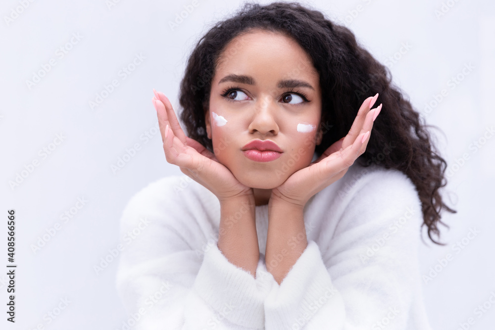 Positive dreamy young mixed race ethnicity girl apply moisturizing cream, make funny face Positive dreamy young mixed race ethnicity girl apply moisturizing cream, make funny face