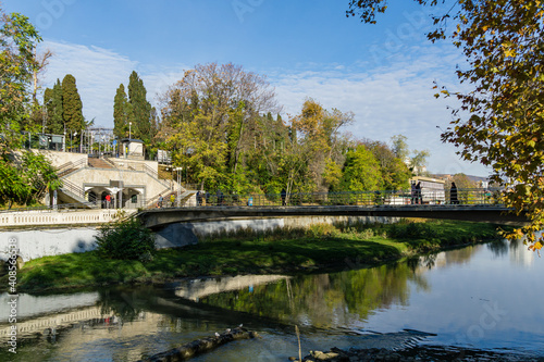 Beautiful autumn view of Sochi river with reflection of sky in water. River embankment with building and pedestrian bridge. Sochi city center. Sochi, Russia - November 23, 2020