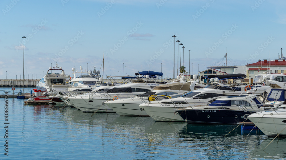 Ships, yachts and boats on blue surface of Black Sea by pier of Commercial seaport of Sochi. Resort city center. Sochi, Russia - November 23, 2020