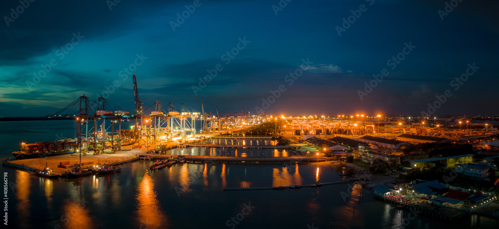 An aerial view at night of a busy port with ship waiting to be filled with containers.
