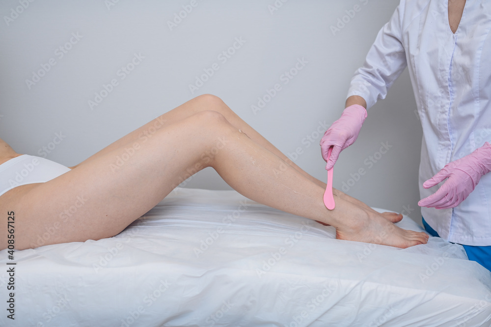 Fototapeta premium Laser epilation and cosmetology in beauty salon, spa concept. Preparation for the procedure of laser hair removal. Application of gel, disposable spatula. Beautiful smooth female legs.