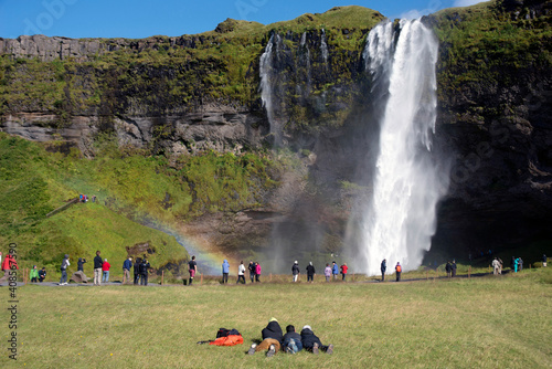 Seljalandsfoss Waterfall surrounded by fields and mountains, rainbow in the mist