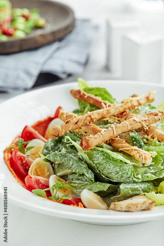 Caesar salad with bread sticks, quail eggs, cherry tomatoes and grilled chicken in plate on white background